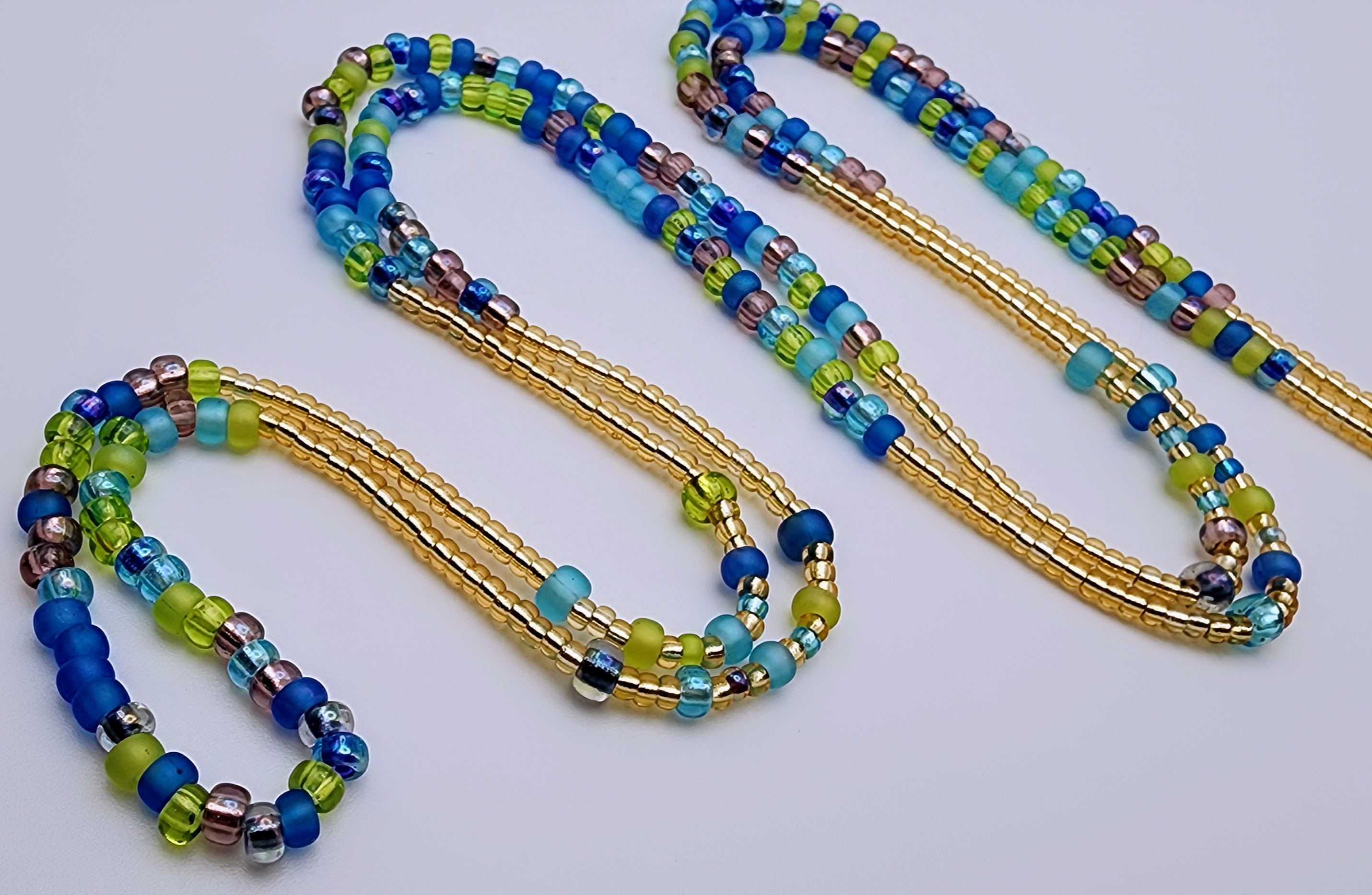 Waist beads made of beads in alternating patterns, featuring green, purple, blue, and gold beads.